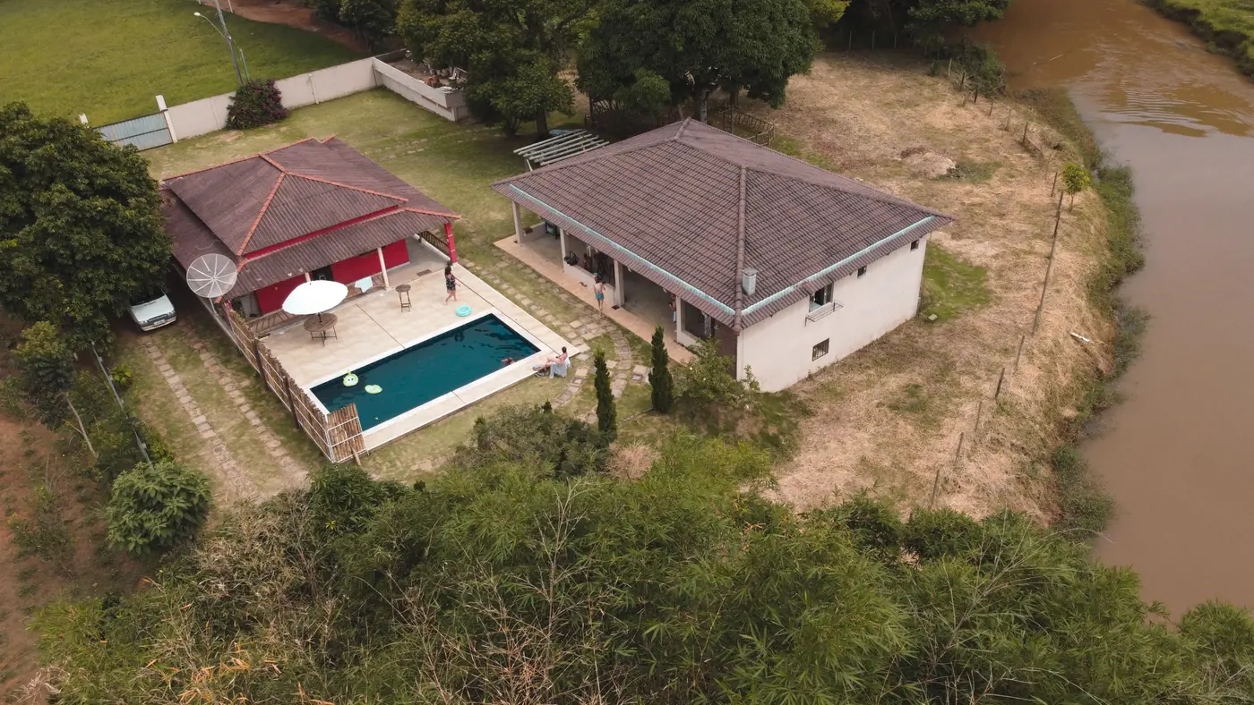 Vista aérea da Rosalinda: casa vermelha, piscina e salão de festas cercados de verde, à beira do rio