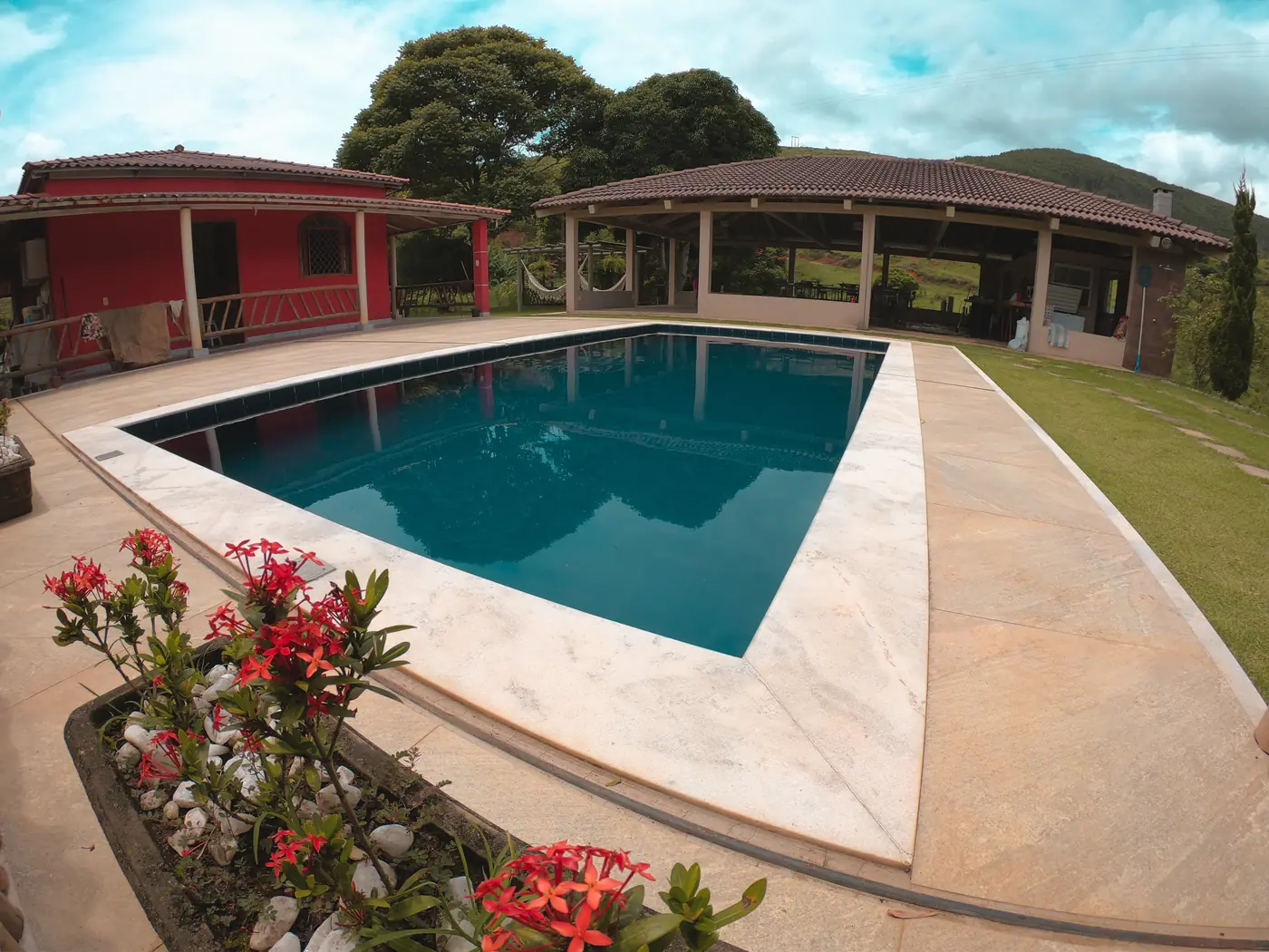 Piscina com borda de mármore e canteiro de flores vermelhas