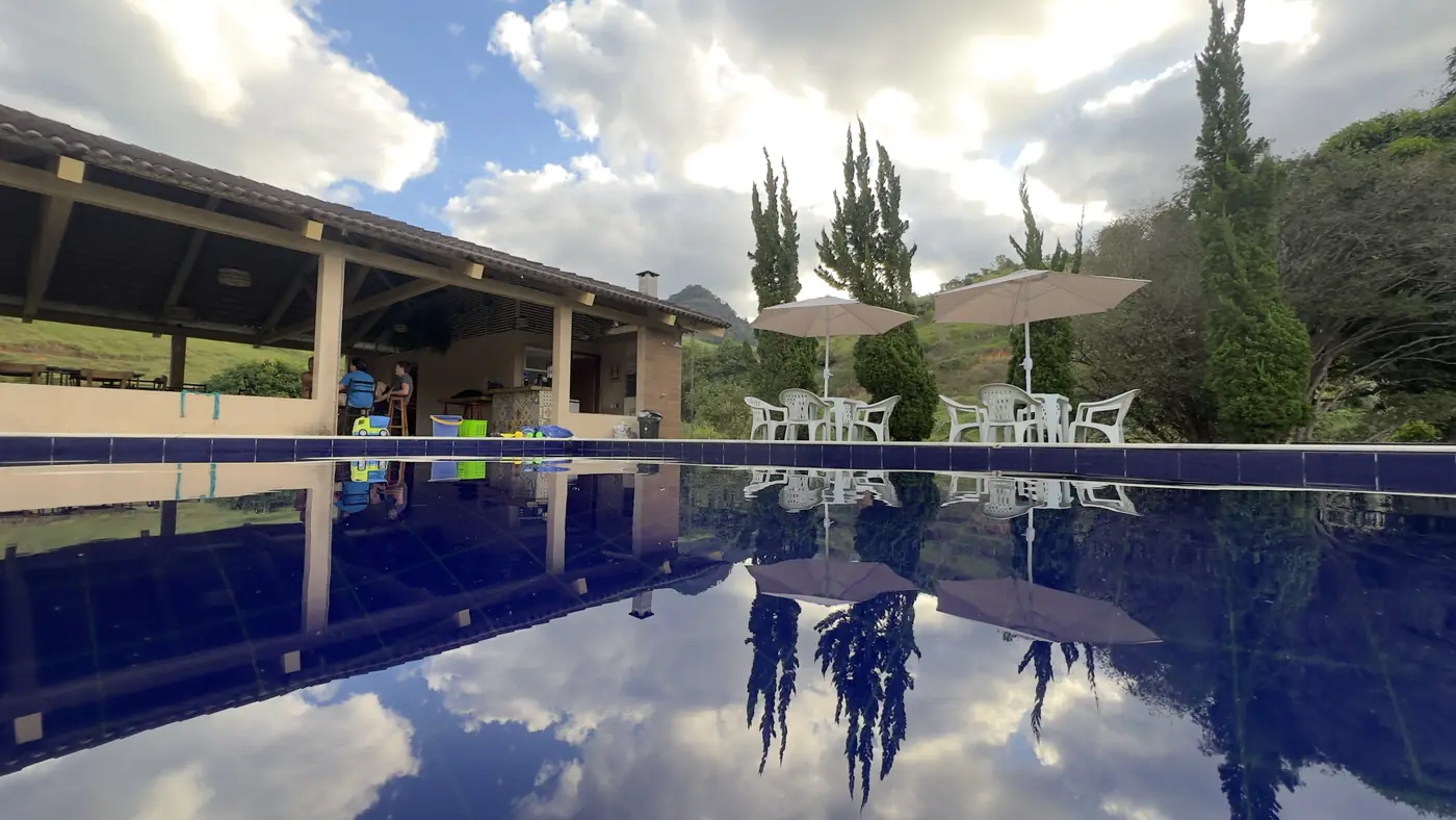 Nuvens e ciprestes refletidos na piscina, com o salão à esquerda