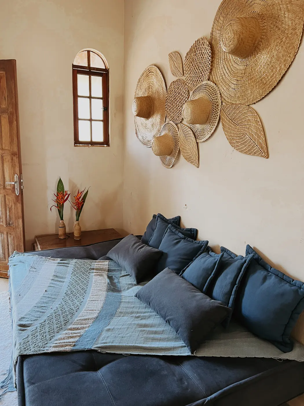 Sala com sofá azul, almofadas e chapéus de palha na parede